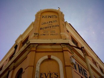 The gable on Kent’s Building, Beach Front, Muizenberg (designed by architect Charles Henry Smith (1863 – 1930) who was best known for his pioneering knowledge of reinforced concrete and fireproofing. Regarding the architectural history of the building, historian Mike Walker writes in a new book that the building was a single story when built in 1916 and extended in 1929 by two floors. EG Holwill bought the draper’s and outfitters business from Michael Kent in the 1930s and possibly the building (to be confirmed). The gable on Kent’s Building, Beach Front, Muizenberg (designed by architect Charles Henry Smith (1863 – 1930) who was best known for his pioneering knowledge of reinforced concrete and fireproofing. Regarding the architectural history of the building, historian Mike Walker writes in a new book that the building was a single story when built in 1916 and extended in 1929 by two floors. EG Holwill bought the draper’s and outfitters business from Michael Kent in the 1930s and possibly the building (to be confirmed).